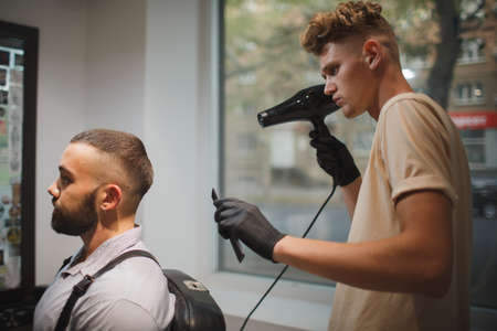 Young barber with a hair spray working on a blurred background. Stylish client in barber shop Barber occupation concept.の写真素材