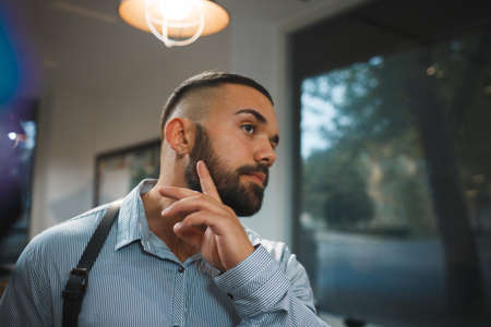 Bearded man on a blurred background. Handsome man touching new beard in a barbershop. Hipster style concept. Copy space.の写真素材