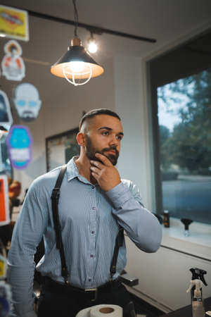 Bearded man on a blurred background. Handsome man touching new beard in a barbershop. Hipster style...