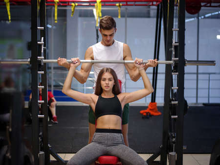 A strong woman with beautiful athletic body doing exercises with a barbell on a gym background. Bodybuilding concept.の写真素材