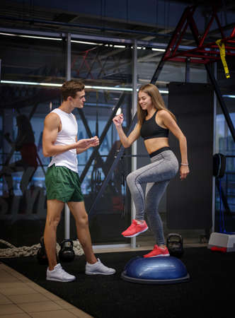 A stunning girl working out with a stepper in a gym background. A woman training with a young coach in a fitness club.の写真素材
