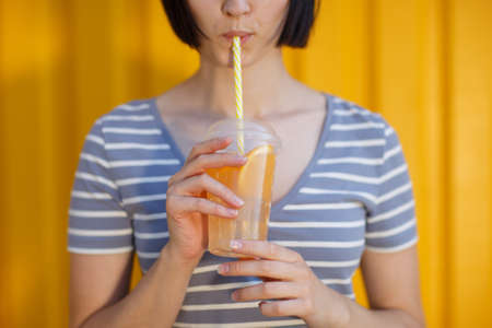 A lovely and charming female holding a refreshing drink with slices of oranges on a yellow background. Healthy concept.の写真素材