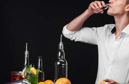 An attractive bartender drinks a beverage, a bar counter with lime, lemon on a dark black background.の写真素材