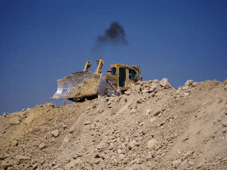 A backhoe loader, a loader backhoe, digger on a heap of sand and stones on a natural background.の写真素材