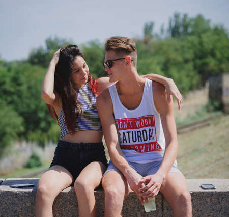 Two positive, cool teens sitting on a natural background. Cute romantic couple in a city park. Romantic leisure concept.の写真素材