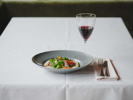A dinner composition on a blurred restaurant background. A tasty dish next to a glass of red wine. Copy space.の写真素材