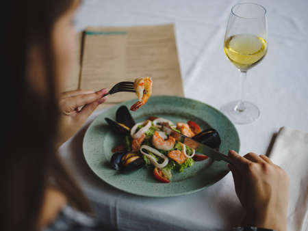 Closeup female eating seafood. A plate of shrimps and a glass of wine on a table background. Restaurant cuisine concept.の写真素材