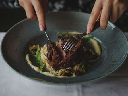 Macro picture of a tasty dish in a blue plate on a white table background. Hand are cutting a piece of juicy meat. Copy space.の写真素材
