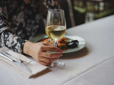 Close-up of a woman at the restaurant. Lady holding wine on a blurred background. Luxurious lunch concept. Copy space.の写真素材