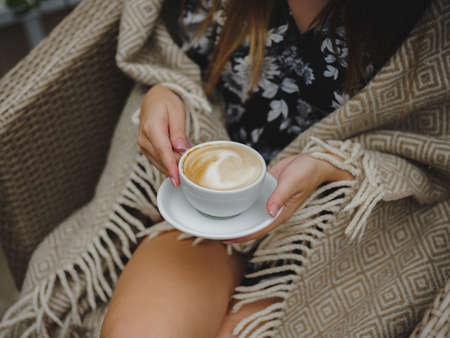 Close-up of a girl drinking coffee. Beautiful latte in a cup. Woman holding served coffee on a blurred cafe background.の写真素材