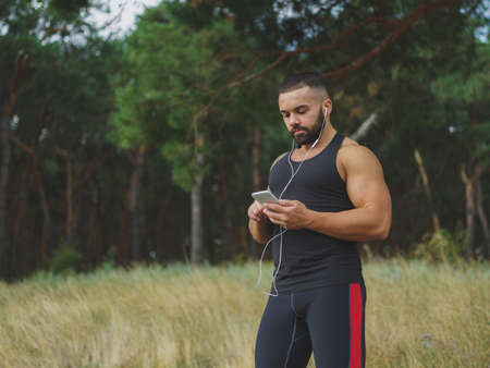 A muscular handsome bodybuilder with a tattoo on his shoulder listening music after a workout on a natural background.の写真素材