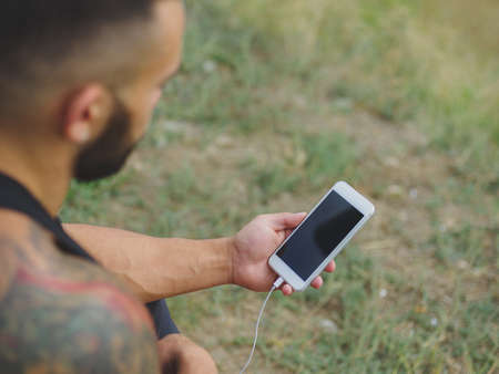Close-up sports man with a phone. Fit athlete after exercise on a natural background. Technology concept. Copy space.の写真素材