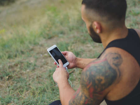 Close-up sports man with a phone. Fit athlete after exercise on a natural background. Technology concept. Copy space.の写真素材