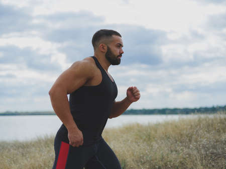 A close-up of a sportive jogger on a natural background. A handsome bodybuilder running outdoors. Sports concept.の写真素材