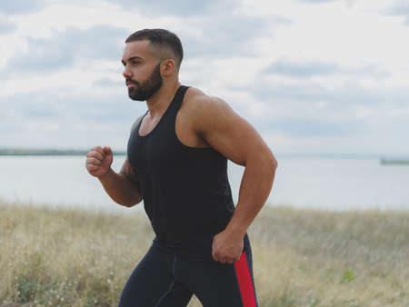 A close-up of a sportive jogger on a natural background. A handsome bodybuilder running outdoors. Sports concept.の写真素材