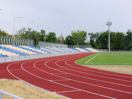 Red treadmills, track running, green grass and empty stands at the stadium, on blue sky. Sport and fitness.の写真素材