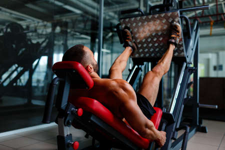 Sexy muscular men using a leg press machine and placing his legs on the platform on a dark colorful background.の写真素材