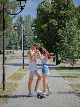 A cute couple of teens dating in a park, riding on a longboard on a natural blurred background.の写真素材