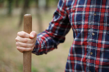 A macro picture of a digging process. A wooden handle of shovel in male hand. A young naturalist planting a tree on a blurred park background. Nature, environment and ecology concept. Copy space.の写真素材