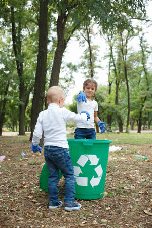 Back of fair boy with hairstyle pigtails. Throwing plastic bag into recycling bin. Land and rubbish on the background.の写真素材