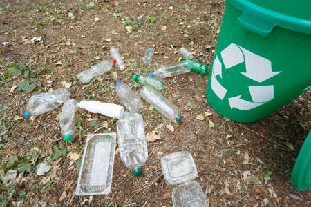 A view from above on a bright green recycling bin in the park. A plastic garbage bin next to plastic bottles and containers on a blurred ground background. Ecology, nature protection concept.の写真素材