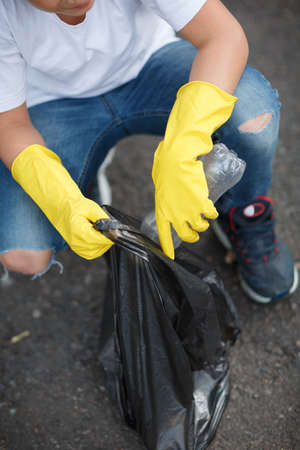 Macro picture of child's legs and hands in yellow latex gloves. Children picking up the plastic trash. Environment, ecology, nature protection, pollution concept. Copy space.の写真素材