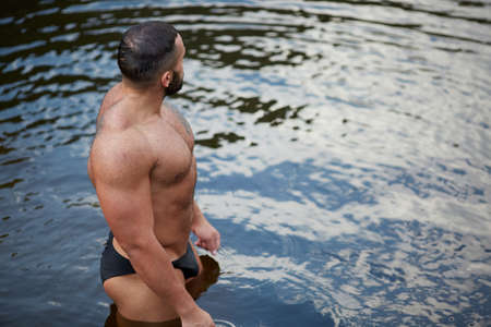 A muscular sexy man in swimming trunks looking into the distance on the sea shore. A swimmer on a...