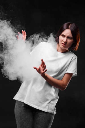 A woman in white T-shirt in an electronic cigarette smoke cloud. A female silhouette on a black background. Copy space.の写真素材