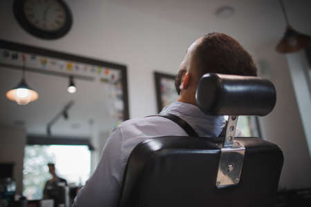A close-up of a handsome man sitting in a hairdressers chair. A young stylish male with a beard in a barbershop.の写真素材