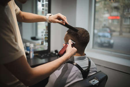 A stylish hairstylist serving client on a barbershop background. Hairdressers hands shaving male clients head. Beauty concept.の写真素材