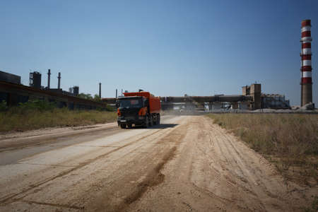 A huge orange tip truck with a shadow driving on a road on a natural background. Huge transporter in...