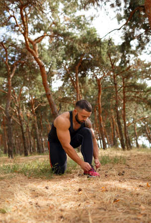 A sporty athlete tying his shoelaces before a training on a natural background. Healthy lifestyle concept. Copy space.の写真素材