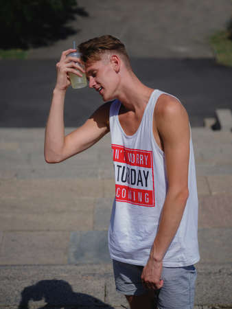 A tired young man with a lemonade on a blurred urban background. A stylish guy outdoors. Summer holiday concept.の写真素材