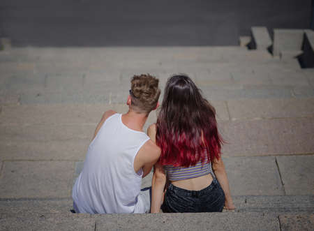 A couple of youngers sitting and looking into the distance on stone stairs background. Relaxation, romance, outdoors concept.の写真素材