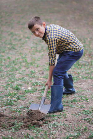 The boy is digging the earth in a park autumn. Person digging in gardenの写真素材
