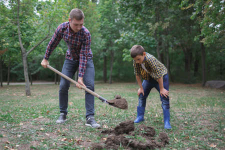 Two brothers a dig earth in a park for planting young tree. Family work, autumn day.の写真素材