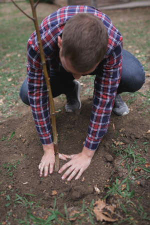 Male has planted a young tree and care about him while working in the garden. Earth day, earth...