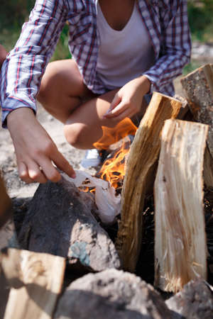 Female camper kindling to start a campfire, bonfire close-up. Man kindles a fire. Fire in nature. Bonfire in the forest.の写真素材
