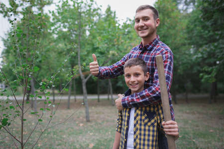 Planting a family tree. Happy young man planting a tree while his little brother helping him. Earth day. We are doing everything together.の写真素材