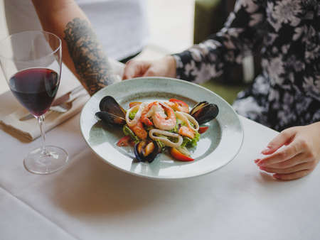 A beautiful dinner composition on a blurred background. A bright plate with tasty seafood dish next...
