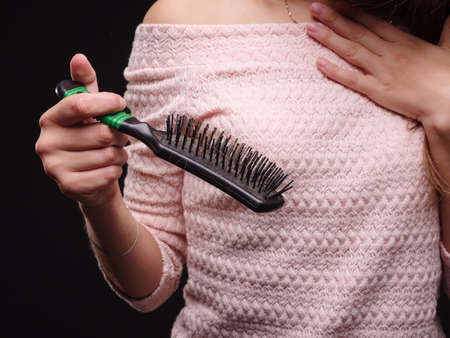 Close-up picture of beautiful woman's hands cleaning a comb from the hair on the black background....