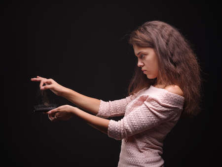 Sad woman holding tangled hair on the black background. Tuft of hair on a girls hand. Hair loss concept. Copy space.の写真素材