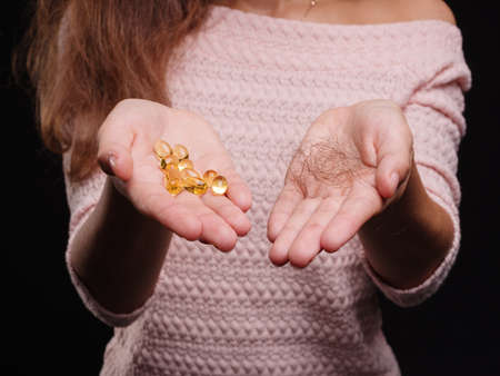 Hands with capsules and tangled hair on a black background. Close-up girl with fish fat pills. Hair treatment concept.の写真素材