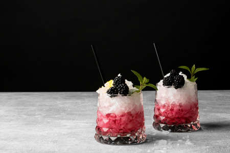 A gray table with two glasses of red, pink beverages and little slices of ice, fresh green leaves of mint, black drinking straw on a black background. Summer sweet drinks.の写真素材