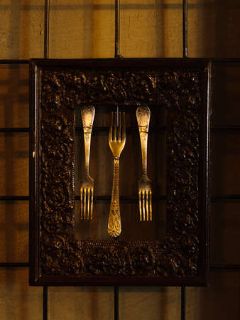 A close-up picture of three old silver forks in a metal frame on a dark wall background. Beautifully framed ancient forks for a kitchen, restaurant or cafeteria decorations.の写真素材