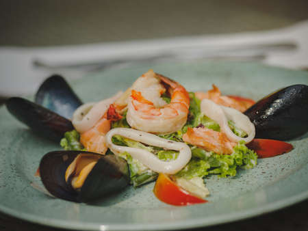 Fresh shrimp, mussel, tomato, salad leaf. Beautiful dish on a large light plate. Professional, seasonal kitchen. Exotic dish in an expensive restaurant. A plate on the table.の写真素材