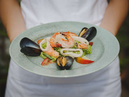 Fresh shrimp, mussel, tomat, salad leaf. Beautiful dish on a large light plate. Professional, seasonal kitchen. Exotic dish in an expensive restaurant. A plate on the hands.の写真素材