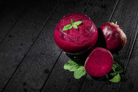 Beautiful dark beetroot cocktail with mint in a transparent glass on a dark wooden background. Natural vegetables and green salads. Healthy restaurant beverages and juices. Copy space.の写真素材