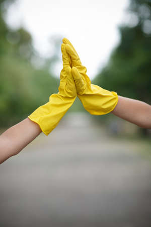 Team work of outdoors cleaning. Environmental protection. Closeup cropped portrait. Getting started cleaning. Yellow rubber cleaning gloves closeup. Workhouse concept. Helping team.の写真素材