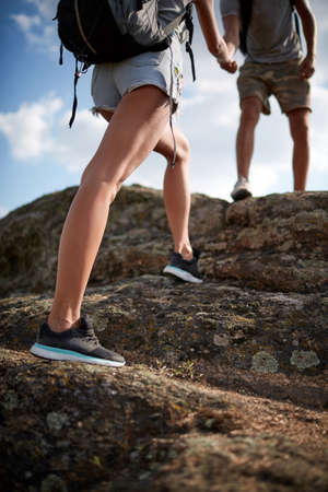 Sport legs. Woman hiker climbing rock on mountain peak cliff, her man giving hand and helping to climb. Assistance. Concept of sport and active life. Help, support, assistance in a dangerous situationの写真素材